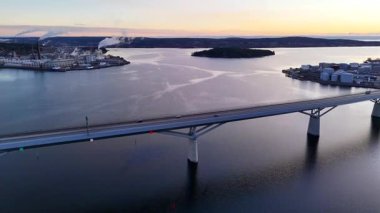 İsveç 'in Sundsvall kentindeki bir köprünün hava görüntüsü, sakin su üzerinde hareket eden araçları gösteriyor, modern yol tasarımı, güvenlik bariyerleri ve temiz yapısal ayrıntıları içeriyor..