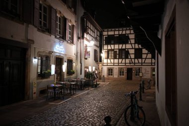 Geceleri Strasbourg Petite France 'da huzurlu kaldırım taşı caddesinde açık kafe koltuklar ve yarı ahşap tarihi binalar bulunuyor.. 