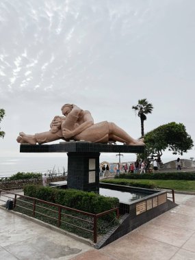 Lima. Peru 12.10.2024 Park del Amor Aşk Parkı 'nda öpüşen bir çiftin ünlü heykeli. Ziyaretçiler bulutlu bir günde arka planda Pasifik Okyanusu 'nun olduğu yakınlarda yürürler.. 