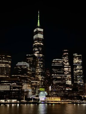 Canlı yeşil kulesi olan bir Dünya Ticaret Merkezi New York şehrinin siluetini aydınlatıyor ve gece boyunca sakin rıhtıma yansıyor.. 