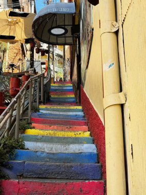 Valparaiso, Şili 11.26.2024 Dar, gökkuşağı boyalı bir merdiven, canlı şehir binaları arasında yukarı doğru esiyor, sıcacık bir kafeye ve bohem bir mahallede yerel tiyatroya çıkıyor..