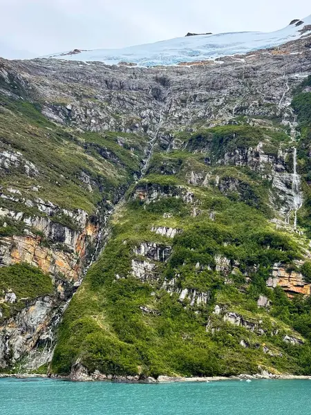 İnce buzul şelaleleri engebeli, yukarıdaki buzlu bir buzuldan orman uçurumlarına akıyor ve aşağıdaki uzak fiyordun canlı turkuaz sularına ulaşıyorlar.. 