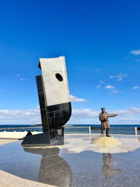 Punta Arenas, Şili 10.22.2023 Bronz denizci heykeli ve gemi yayı heykeli olan modern bir deniz heykeli açık mavi gökyüzünün altında yansıtıcı bir plazada duruyor..
