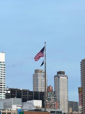 Amerikan bayrağı, açık mavi gökyüzünde çağdaş gökdelenlerin arka planında belirgin bir şekilde dalgalanıyor. Bu, şehir Amerika 'sında vatanseverliği simgeliyor..