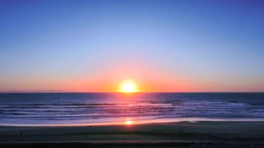 Drone, kum tepeciğinin arkasından pürüzsüz bir şekilde yükselir ve arka planda pembe bir günbatımı gökyüzü ve derin mavi bir okyanusu ortaya çıkarır. Sakin, renkli ve sinematik bir kıyı anı yumuşak ışıkla yakalanır.. 