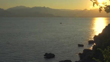 Sakin deniz ve siluetli dağların üzerinde dramatik bir şekilde gün batımını hızlandırdı. Su ve engebeli kıyı şeridi boyunca altın yansımalar yarattı..