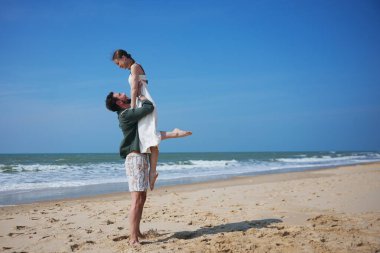 Erkekler, kumlu bir sahilde açık gökyüzü ve okyanus dalgalarıyla neşeli, romantik bir anda kadınları kaldırır. Bu neşeli ve tasasız sahne yaz aşkı ve seyahat titreşimlerini yakalar..