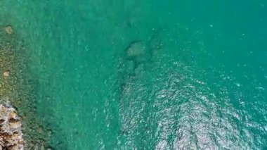 Şeffaf turkuaz deniz suyunun yüksek çözünürlüklü hava görüntüsü, sualtı güneş ışığı yansımalarını gösteriyor, seyahat görselleri için sakin ve tropikal bir kıyı ortamını çağrıştırıyor 