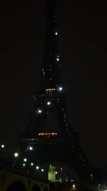 Eyfel Kulesi 'nin dramatik bir gece manzarası. Çok az ışıklandırması var. Sadece parlak ışıklar görünüyor.. 