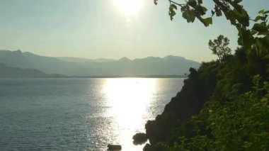 Altın günbatımı sahili kayalar, uzak dağlar ve yeşil ağaçlarla aydınlatır, doğa, seyahat ve manzara içeriği için mükemmeldir.. 