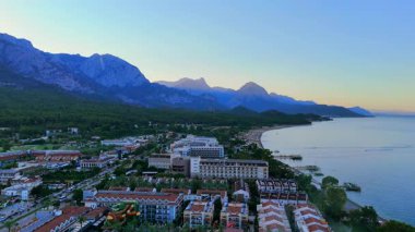 Antalya sahil şeridinin insansız hava aracı panoraması. Sahil, tatil beldeleri ve sakin sabah ışığı ve sakin deniz altında dramatik sıradağlar.. 