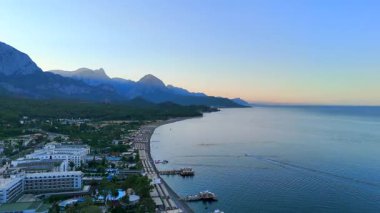 Antalya manzaralı deniz manzarası, orman, dağ siluetleri, sakin deniz ve altın gün ışığı altında otel rıhtımları.. 