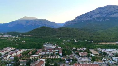 Sabahın erken saatlerinde Antalya 'da yeşil bahçeler, orman tepeleri ve kayalık dağlarla çevrili sakin bir yerleşim yeri manzarası..