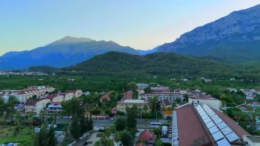 Antalya 'daki bir sahil beldesinin insansız hava aracı görüntüsü sabahın erken saatlerinde oteller, ormanlar, plajlar ve dramatik dağ arkaplanlarını gösteriyor..