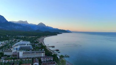Antalya sahilinin havadan görünüşü dinlenme yerleri, rıhtımlar, dağlar ve gün doğumunda gün ışığıyla aydınlanan sakin deniz.. 