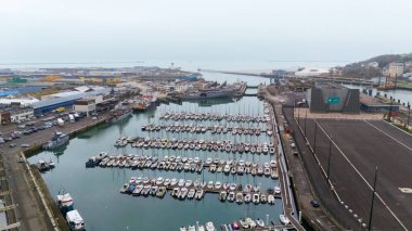 Boulogne. Fransa 03.28.2025 Deniz kenarındaki bir sanayi limanı ve kentsel altyapının yanında bulunan teknelerle dolu bir marinanın yüksek açılı fotoğrafı.. 