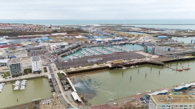 Boulogne. Fransa 03.28.2025 Modern bir marina, kentsel binalar, tersane tesisleri ve bulutlu gökyüzü altında sakin bir kıyı şeridi boyunca uzanan liman alanlarının insansız hava aracı fotoğrafı