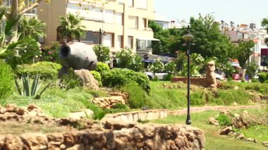 Antalya, Türkiye 04.11.2025 Yeşil şehir parkı, güneş ışığı altındaki ahşap bir köprü, piknik masası, ağaçlar ve yakınlardaki konut binalarının yer aldığı uçurum kenarında yer alıyor.. 