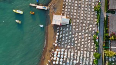 İnsansız hava aracı plaja paralel uçar, şezlonglar, şemsiyeler, rıhtımlar ve kristal berrak turkuaz sularda kayıklar yakalar, yaz titreşimlerini uyandırır..