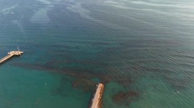 Güneş yatakları, yüzücüler, renkli tekneler ve turkuaz sularda bir rıhtım olan iyi düzenlenmiş bir sahilin insansız hava aracı görüntüsü..
