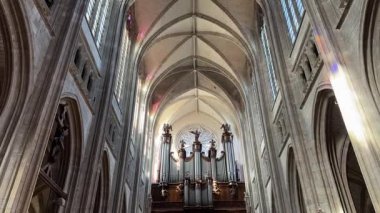 Boru organı, yükselen kemerlerle çerçevelenmiş ve görkemini artıran renkli cam yansımalarla yıkanmış Gotik bir katedralin kubbesinde duruyor. Orlean, Fransa 4.13.2025 