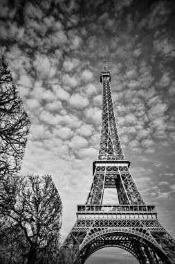 Kışın bulutlu bir gökyüzünün altında Eyfel Kulesi 'nin tek renkli fotoğrafı. Paris ikonik simgesi, mimari ayrıntılar, dramatik ve karamsar atmosfer, dikey yönelim.