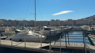 Tekneler Marsilya, Fransa 'daki Vieux limanında demirli. Arka planda Notre Dame de la Garde Bazilikası görülüyor, açık mavi gökyüzünün altında şehir binalarının üzerinde yükseliyor.. 