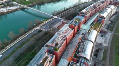 Fransa 'nın Lyon kentindeki modern bir iş bölgesinin havadan görünüşü 04.30.2025, kırmızı binalar, yeşil çatılar, ve yakındaki köprüleri ve yaya geçitleri olan bir nehir.
