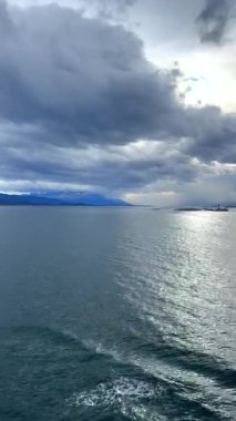 Bulutlu gökyüzünün altında, Tierra del Fuego 'da denizden yansıyan güneş ışığıyla ıssız bir adanın hareket eden yolcu gemisinden görüntü..