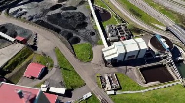 Kömür deposu, boru hatları, tortu tankları ve otoyol yakınındaki fabrika binaları olan bir sanayi bölgesinin insansız hava aracı görüntüsü..