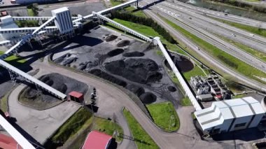 Endüstriyel bir bölgede büyük bir kömür işleme ve depolama tesisi, taşıma bantları ve yakındaki otoyollarla insansız hava aracı görüntüsü.