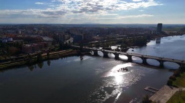 İspanya, Badajoz 'un nehir kenarındaki yeşillikleri, Guadiana nehrinin yansımaları ve şehrin üzerine yumuşak gün ışığı.