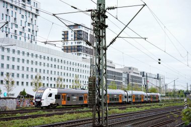 Düsseldorf, Almanya 05.22.2025 Çift katlı banliyö treni, bulutlu bir günde arka planda çağdaş yüksek binalar bulunan elektrikli tren rayları boyunca gider.