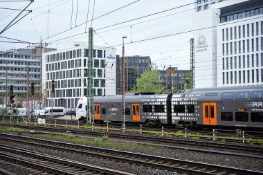 Düsseldorf, Almanya 05.22.2025 Çift katlı banliyö treni modern ofis binaları ve bulutlu bir günde arka planda kablolar ile tren raylarından geçiyor.