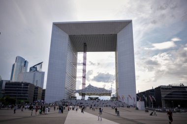 La Defense Paris 'te Büyük Kemer önünde yürüyen ve toplanan insanların geniş açılı görüntüsü. Fransa 06.01.2025 modern ofis binaları ve arka planda dramatik gökyüzü.