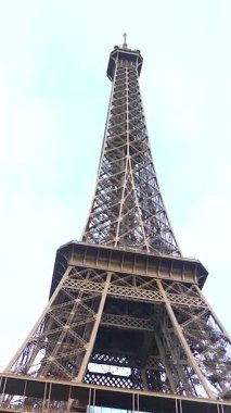 Paris 'teki Eyfel Kulesi' nin dramatik alçak açılı görüntüsü. Soluk, bulutlu bir gökyüzüne ayarlanmış karmaşık demir kafes ve kule şeklini sergiliyor..