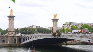 Paris, Fransa 06.07.2025 Pont Alexandre III 'ün süslü heykelleri, altın heykelleri ve aşağıdaki nehir trafiği ile panoramik çekimi, turistler bulutlu bir günde yürürken ve gezerken.