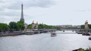 Paris, Fransa 06.07.2025 Paris 'teki Seine Nehri' nin geniş panoramik manzarası turist botları, arka planda Eyfel Kulesi ve dramatik bulutlu gökyüzünün altında süslü Pont Alexandre III köprüsü..