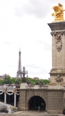 Paris, Fransa 06.07.2025 Paris 'teki süslenmiş Pont Alexandre III köprüsünün manzarası ve bulutlu gökyüzünün altından yükselen Eyfel Kulesi..