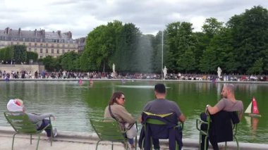 Paris, Fransa 06.07.2025 Jardin des Tuileries 'deki Büyük Havzanın keyfini çıkaran insanların panoramik görüntüsü, yeşil sandalyeler, gölette oyuncak yelkenliler, merkez bir çeşme ve arka planda ağaçlar..
