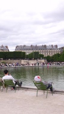 Paris, Fransa 06.07.2025 Jardin des Tuileries 'deki çeşmenin etrafında eğlenen insanların panoramik manzarası, yeşil sandalyeler, canlı bir hava ve bulutlu gökyüzü..