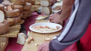 Açık hava pazarında yapılan tatma oturumunda ellerin çeşitli peynirleri dilimleyip tahta bir tahtanın üzerinde ısırık büyüklüğünde numunelere dönüştürmesi..