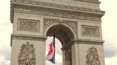 Paris 'teki Zafer Takı Anıtı' nın geniş manzarası. Tarihi taş kemerin altındaki rüzgarda dalgalanan Fransız üç renkli bayrağı..