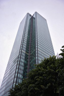 La Defense 'daki modern cam kule, modern mimarisi ve çelik yapısı olan yumuşak bulutlu gökyüzünün altındaki yeşil ağaçların üzerinde yükseliyor.