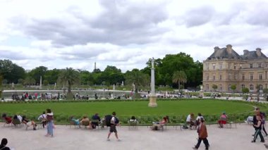Kalabalık, Paris 'teki Lüksemburg Bahçeleri' nde güneşli bir günün tadını çıkarıyor. Gölün etrafında ve tarihi sarayın yakınında oturuyorlar. Sadece editörler kullanır. Haziran 2025.