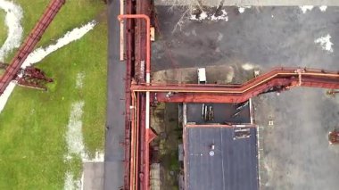 Üst-alttaki dron görüntüsü, çimenli zeminde karla kesişen paslı boru hatlarını gösteriyor, endüstriyel geometri ve uzaysal kontrastı vurguluyor..