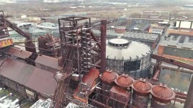 Paslı metal tankların, iskelelerin ve şehrin arka planında yeniden geliştirilmiş endüstriyel bir kompleksin dairesel bir salonunun insansız hava aracı görüntüsü. 