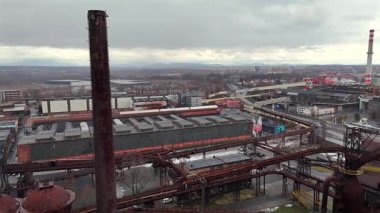 Uzak dağ siluetlerine karşı kurulmuş fabrika çatıları, bacaları, boru hatları ve konut binaları olan sanayi bölgesinin geniş hava manzarası 
