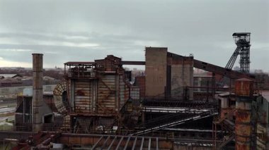 Eski endüstriyel bir alanda paslı taşıma sistemlerinin ve çelik iskeletinin düşük açılı drone görüntüsü yapısal detayları ve kentsel dönüşüm elementlerini gösterir