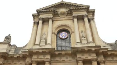 Paris 'teki Saint-Roch Kilisesi' nin tarihi cephesinin yakın görüntüsünde barok sütunlar, taş heykeller ve ana girişin üzerinde büyük bir saat yer alıyor..